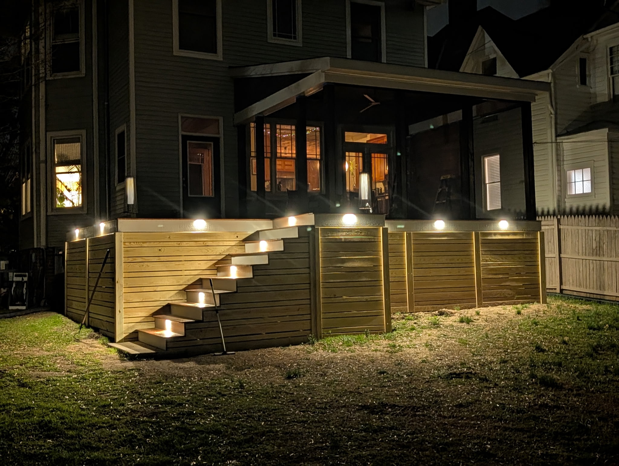 Completed deck and screened porch illuminated at night with integrated stair and perimeter lighting
