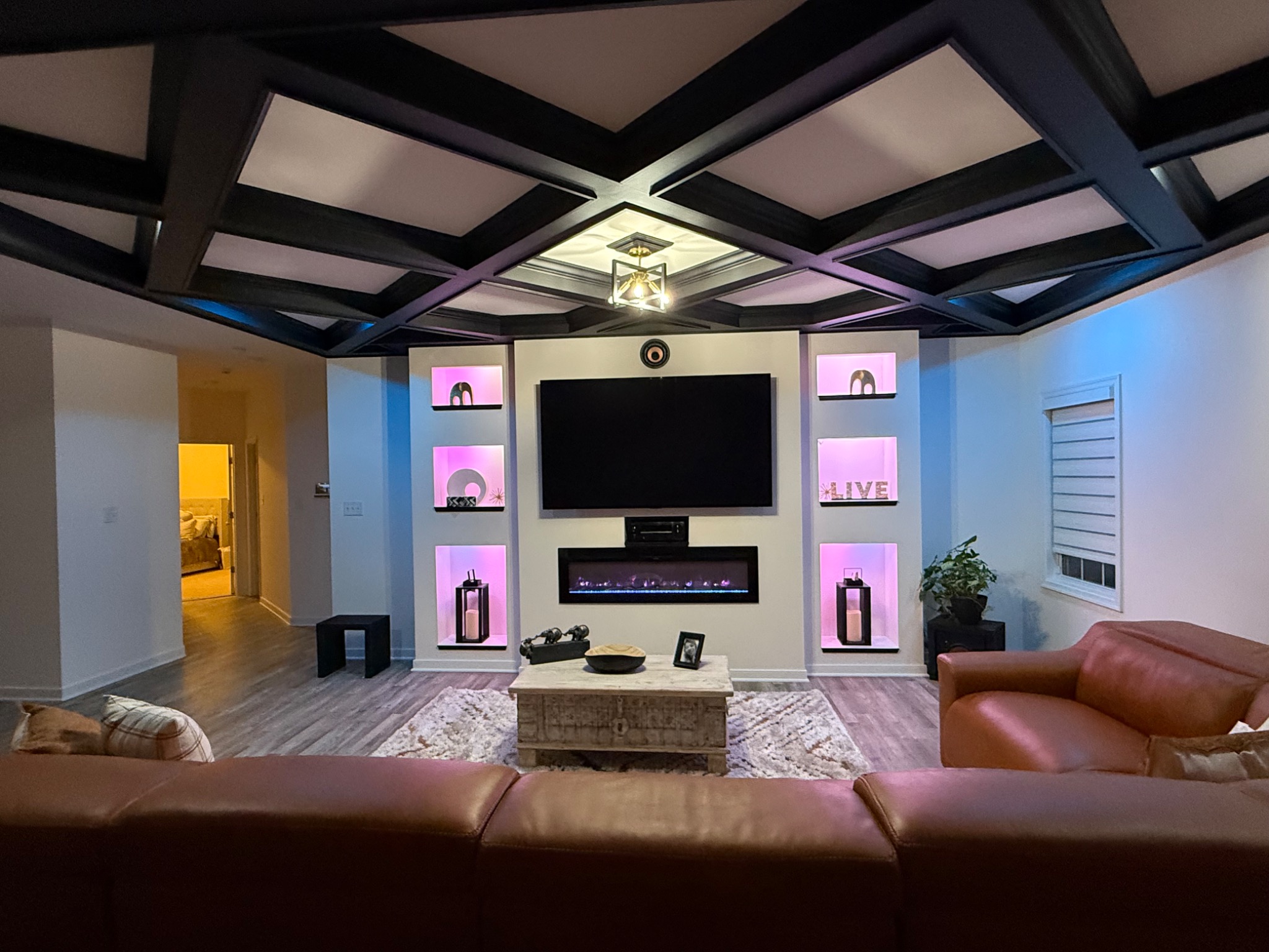 Completed living room upgrade with custom entertainment wall, electric fireplace, illuminated display niches, and black coffered ceiling