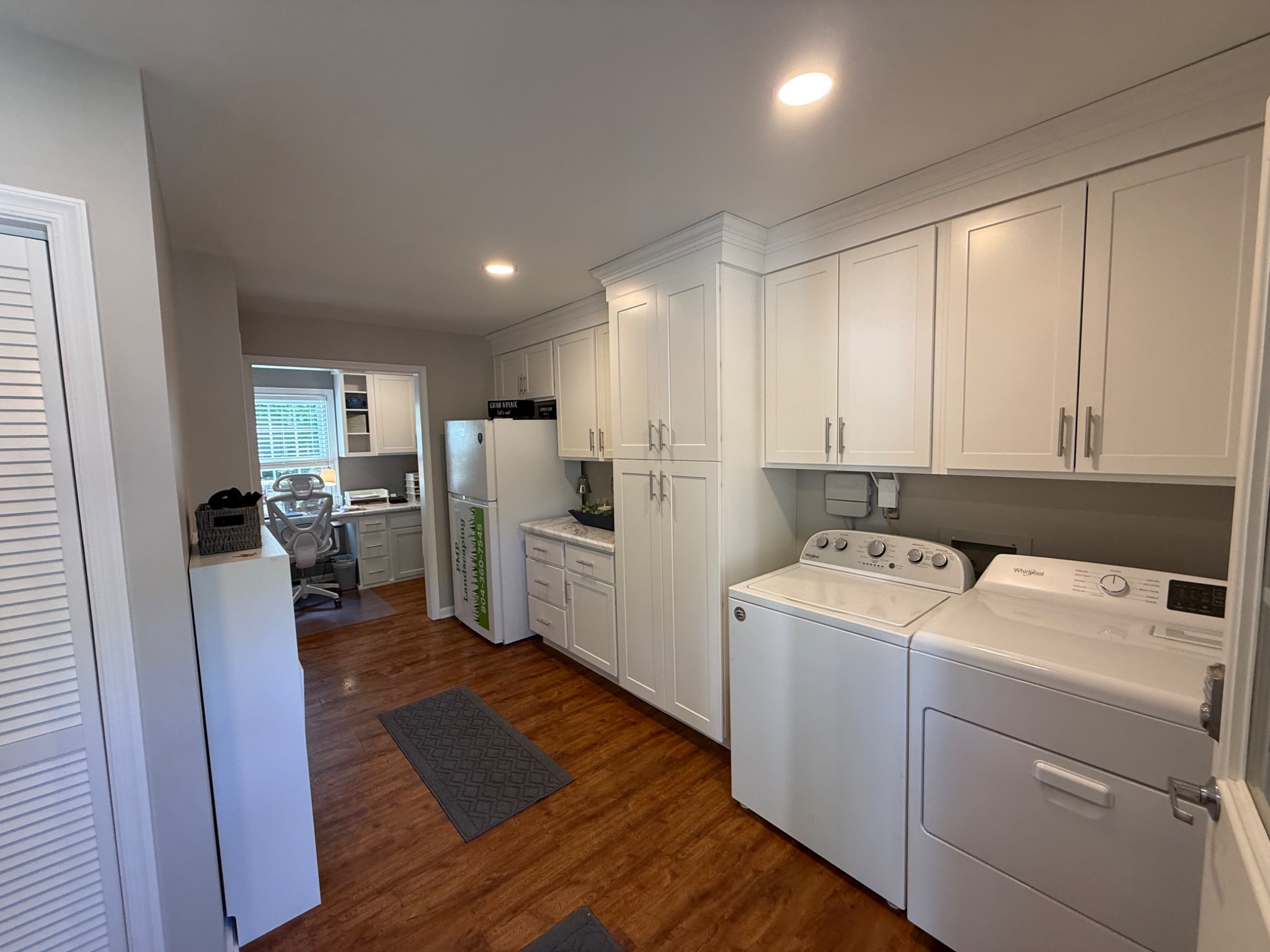Finished laundry and storage room with white cabinetry and wood-look flooring