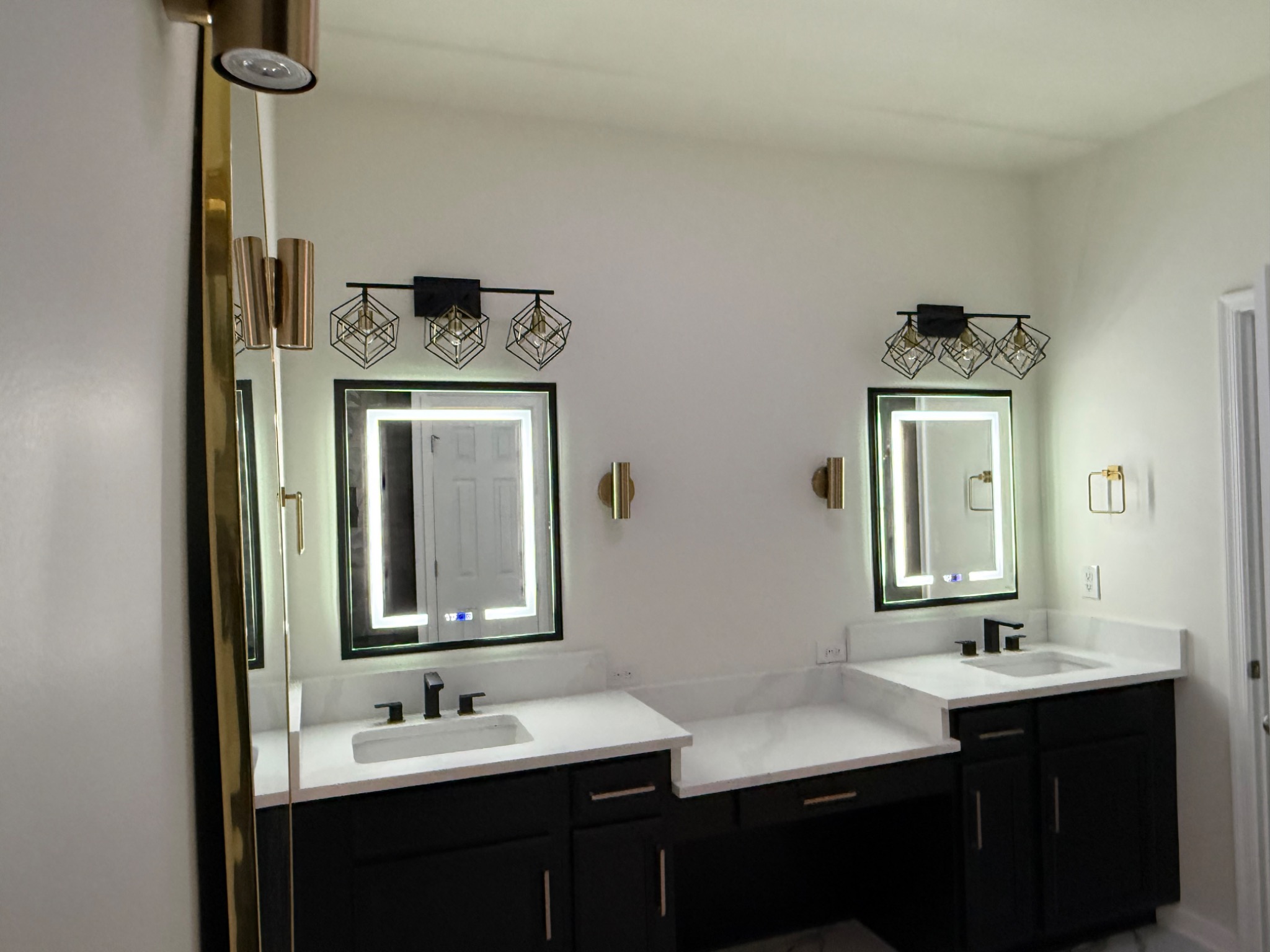 Completed primary bathroom renovation with double vanity, quartz countertops, illuminated mirrors, and modern lighting