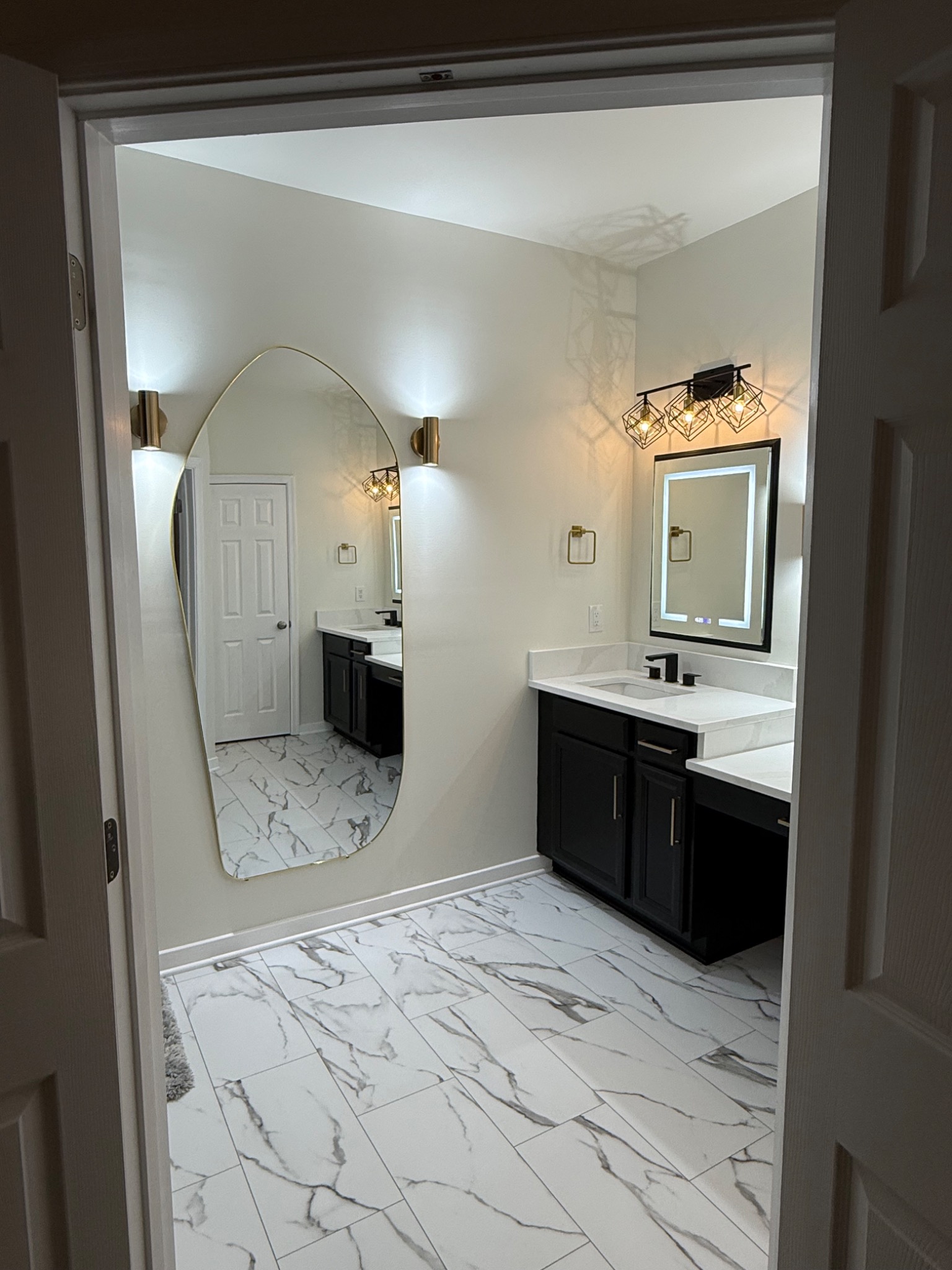 Completed primary bathroom viewed through doorway with marble-look tile and custom vanity