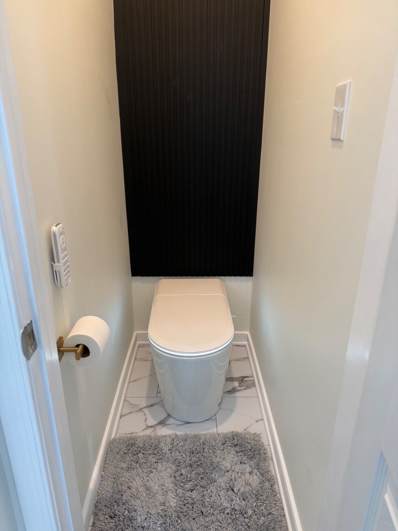 Finished private toilet area with marble-look floor tile and black accent wall