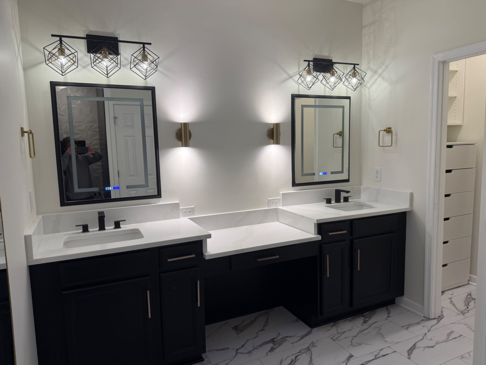 Finished primary bathroom double vanity with black cabinetry, white quartz, illuminated mirrors, and modern lighting